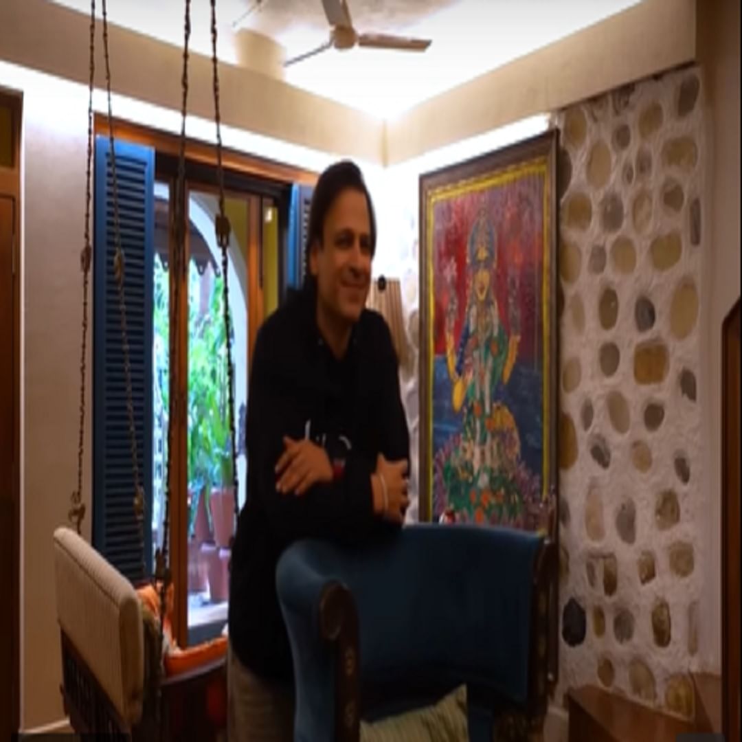  लिव्हिंग एरियामध्ये उत्कृष्ट लाकडी फर्निचर आहे , जे घराला आकर्षक आणि विंटेज लूक देण्यास मदत करते. खिडक्या देखील लायनिंग पॅटर्नमध्ये डिझाइन केल्या आहेत, ज्या निळ्या रंगाने हायलाइट केल्या आहेत. माता लक्ष्मीची एक मोठी प्रतिमा देखील आहे आणि त्याच रंगाच्या लाकडात डिझाइन केलेला दिवा आहे. त्याची सुंदर रचना सर्वात जास्त आकर्षित करते.