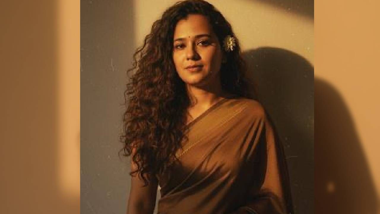 चॉकलेटी रंगाच्या साडीसाठी Prompt : create a vintage grainy but bright image of the reference picture but draped in a perfect brown color pinteresty aesthetic retro saree. It must feel like like a 90’s movie with long hair with a small flower tucked visibly into her curls and romanticising the windy enviroment. The girl is standing against a solid wall deep shadows and contrast drama creating a mysterious and artistic atmosphere where the lighting is warm with golden tones of evoking a sunset or golden hour glow . The background is minimalistic and slightly textured and the expression on her face is moody calm yet slightly happy and introspective हे पेस्ट करा.