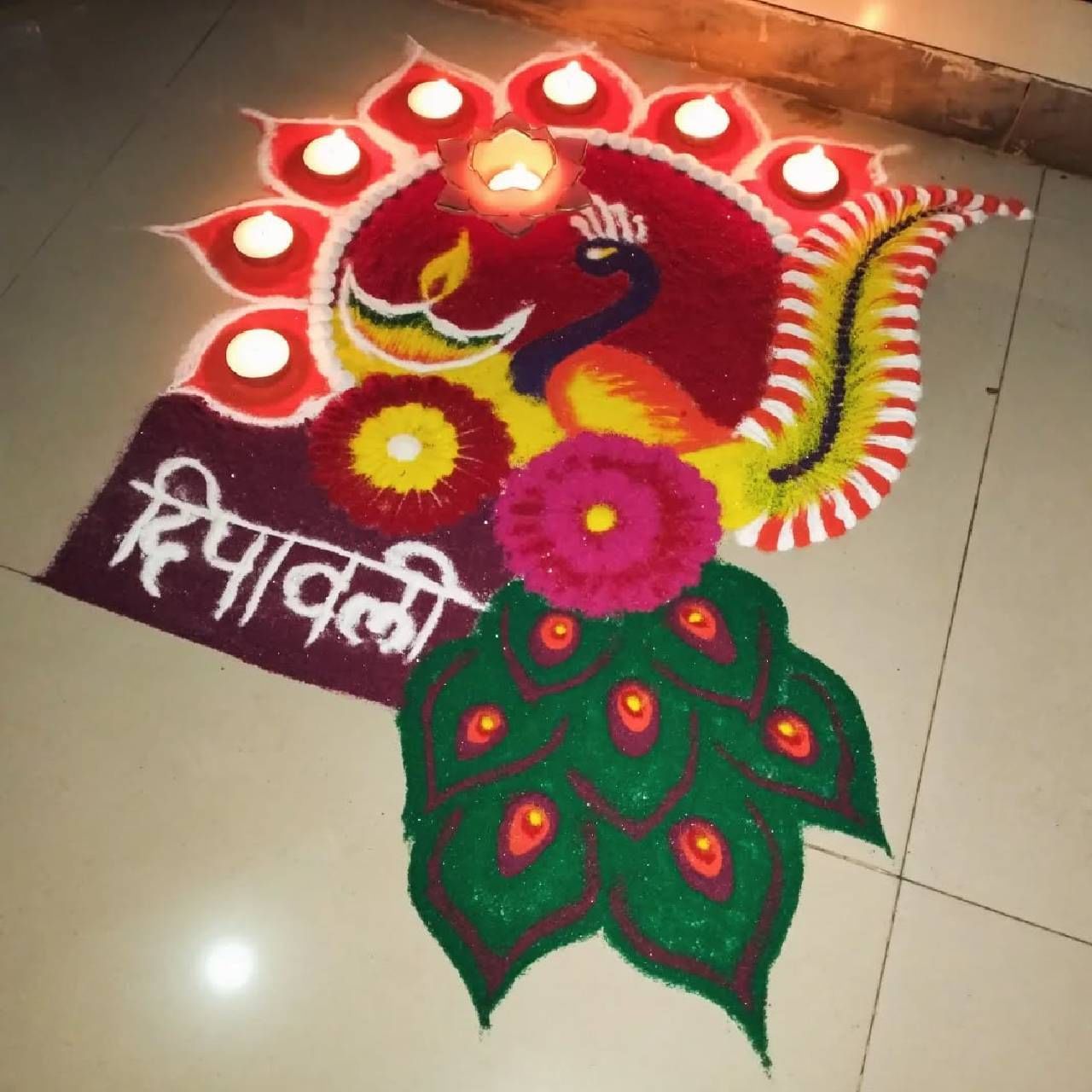  या रांगोळीतही मोराचे सुंदर चित्र आणि फुलांचे  आकर्षक नक्षीकाम पाहायला मिळत आहे. या रांगोळीत चौकोनी आकारात दीपावली असे लिहिण्यात आले आहे. यात दिव्यांच्या आणि मोरपंखांच्या डिझाईनचा वापर करून तयार केलेली ही रांगोळी फारच आकर्षक आणि कलात्मकतेला महत्त्व देणारी आहे.