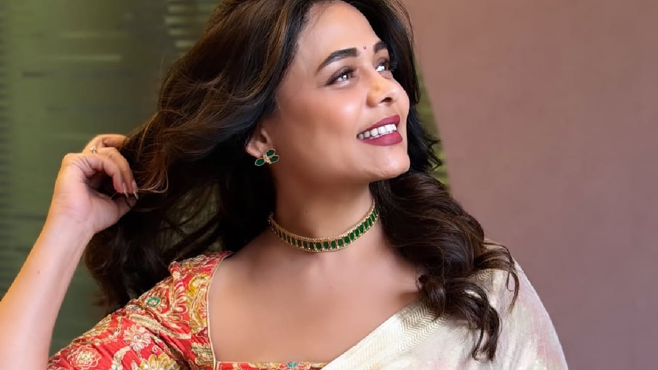 हिरव्या आणि सोनेरी मोत्यांचा चोकर, मोकळे केस आणि साधा मेकअप यामुळे तिच्या पारंपरिक सौंदर्यात अधिक भर पडली आहे.