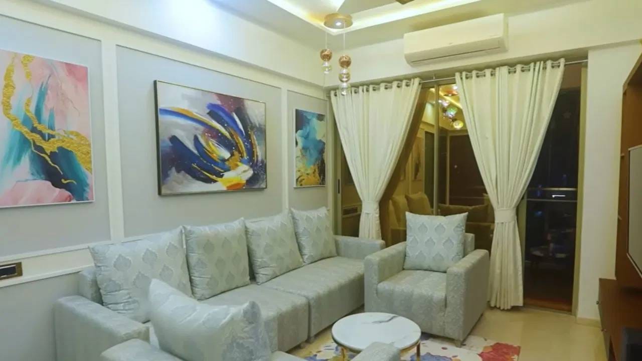 घरातील लिव्हिंग रूम म्हणजे एलिगन्सचा परफेक्ट नमुना! पांढऱ्या आणि ग्रे रंगातील म्युटेड सोफे, भिंतींवरील आकर्षक पेंटिंग्स आणि मिनिमल सजावट यामुळे संपूर्ण रूमला प्रीमियम लूक मिळतो.