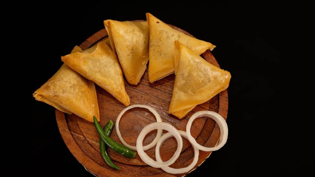 समोसा भारतात लोकप्रिय असला तरी, त्याचा इतिहास मध्य आशिया आणि पर्शियाशी जोडलेला आहे. इतिहासकारांच्या मते, हा पदार्थ व्यापारी आणि प्रवाशांच्या माध्यमातून भारतीय उपखंडात पोहोचला. काळानुसार स्थानिक आवडीनिवडीनुसार त्यात बदल होत गेले आणि बटाटे, वाटाणे व मसाल्यांनी बनवलेल्या समोशाने भारतीय खाद्यपदार्थांमध्ये एक विशेष स्थान मिळवले आहे.